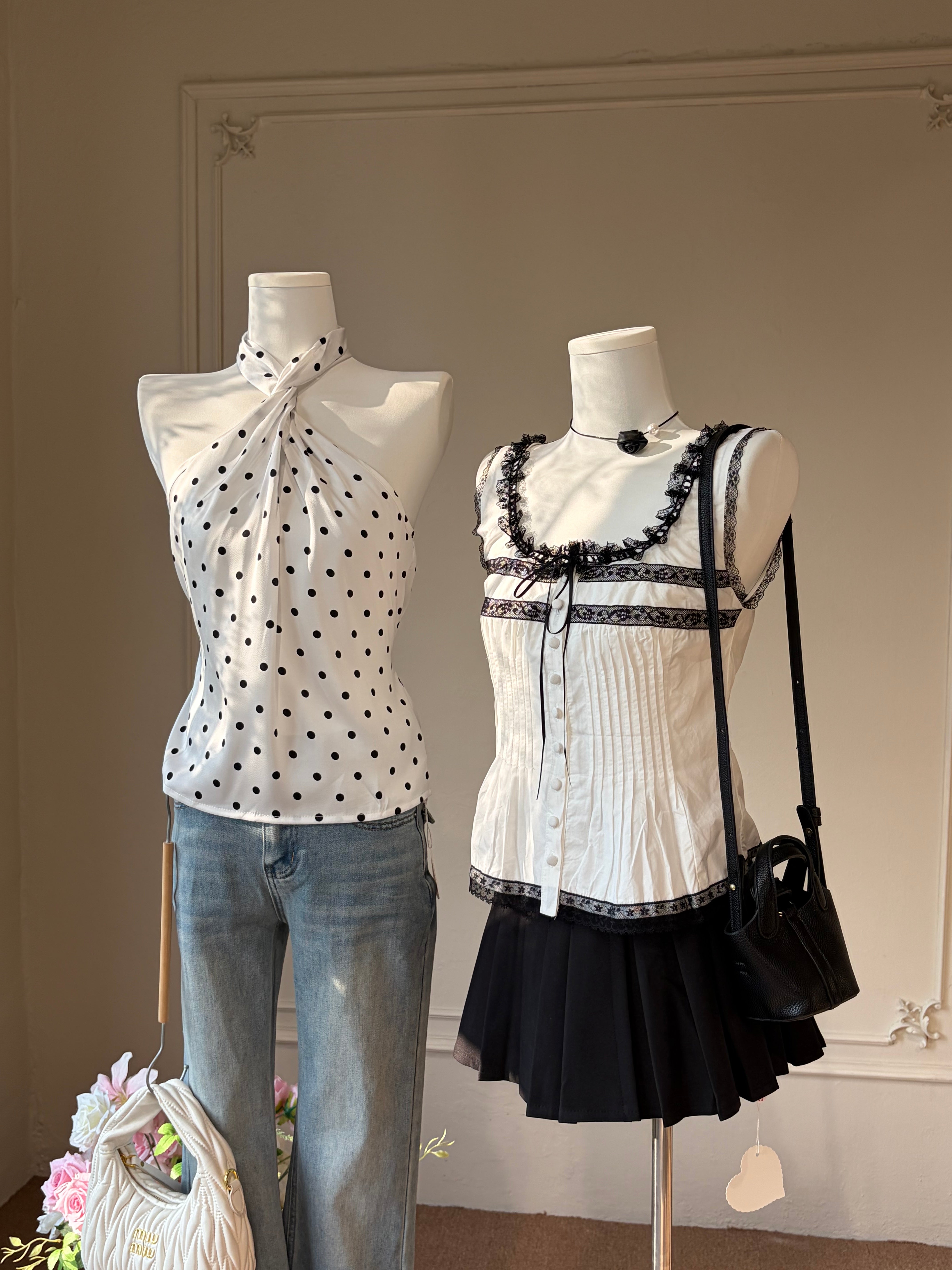 Two mannequins display women's outfits in an indoor room. The left mannequin wears a white halter top with black polka dots and light blue jeans.Charme.cc