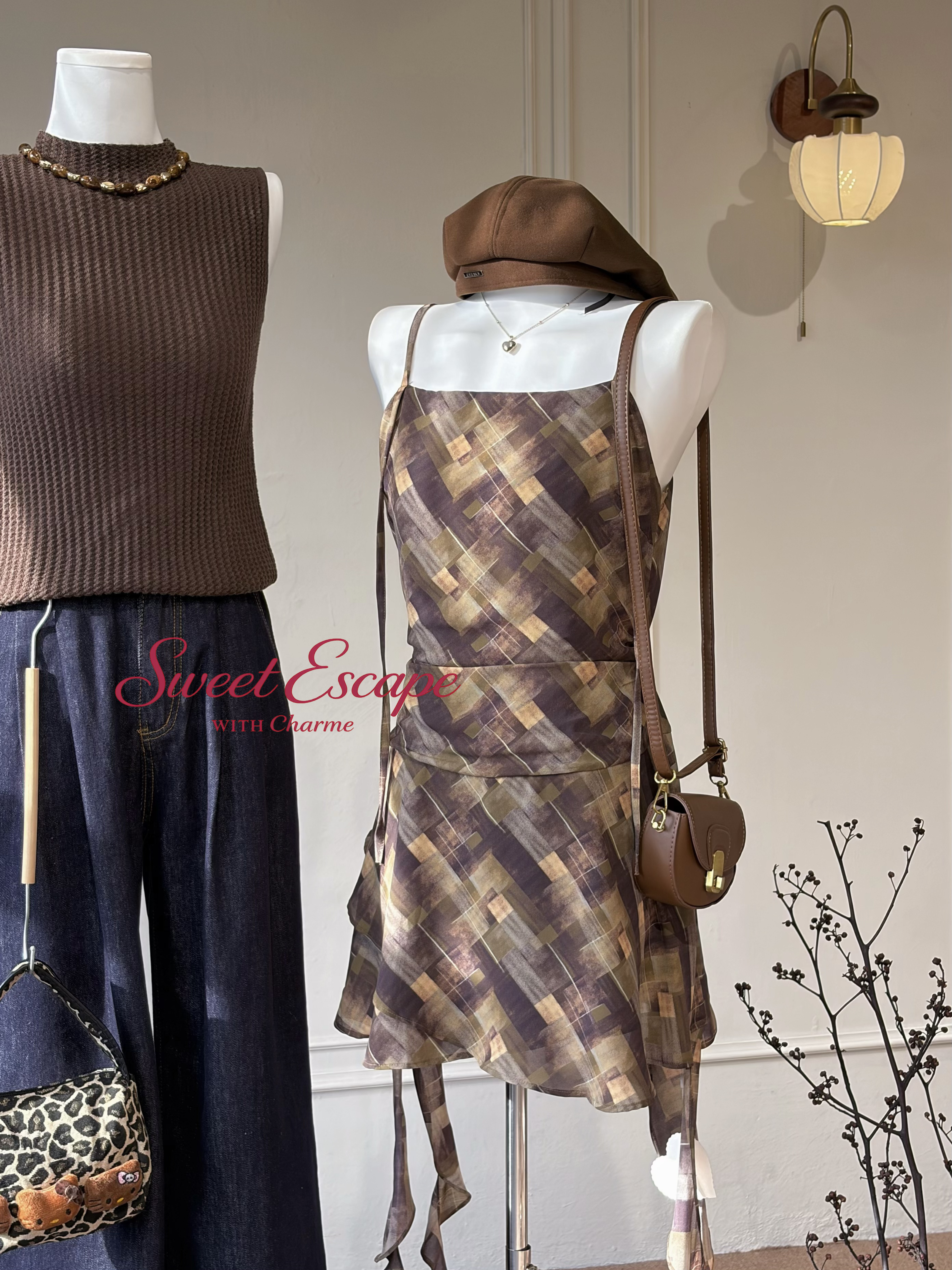 Mannequins wearing a patterned dress, brown sweater, and blue pants with accessories in a store setting.