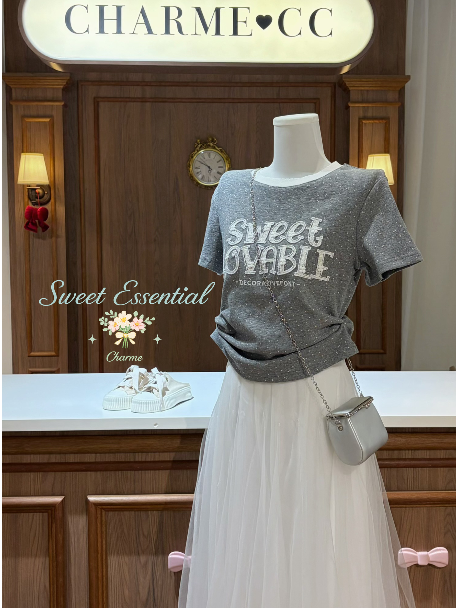 Mannequin wearing a gray 'Sweet Lovable' shirt with a white skirt and silver handbag in a store setting.
