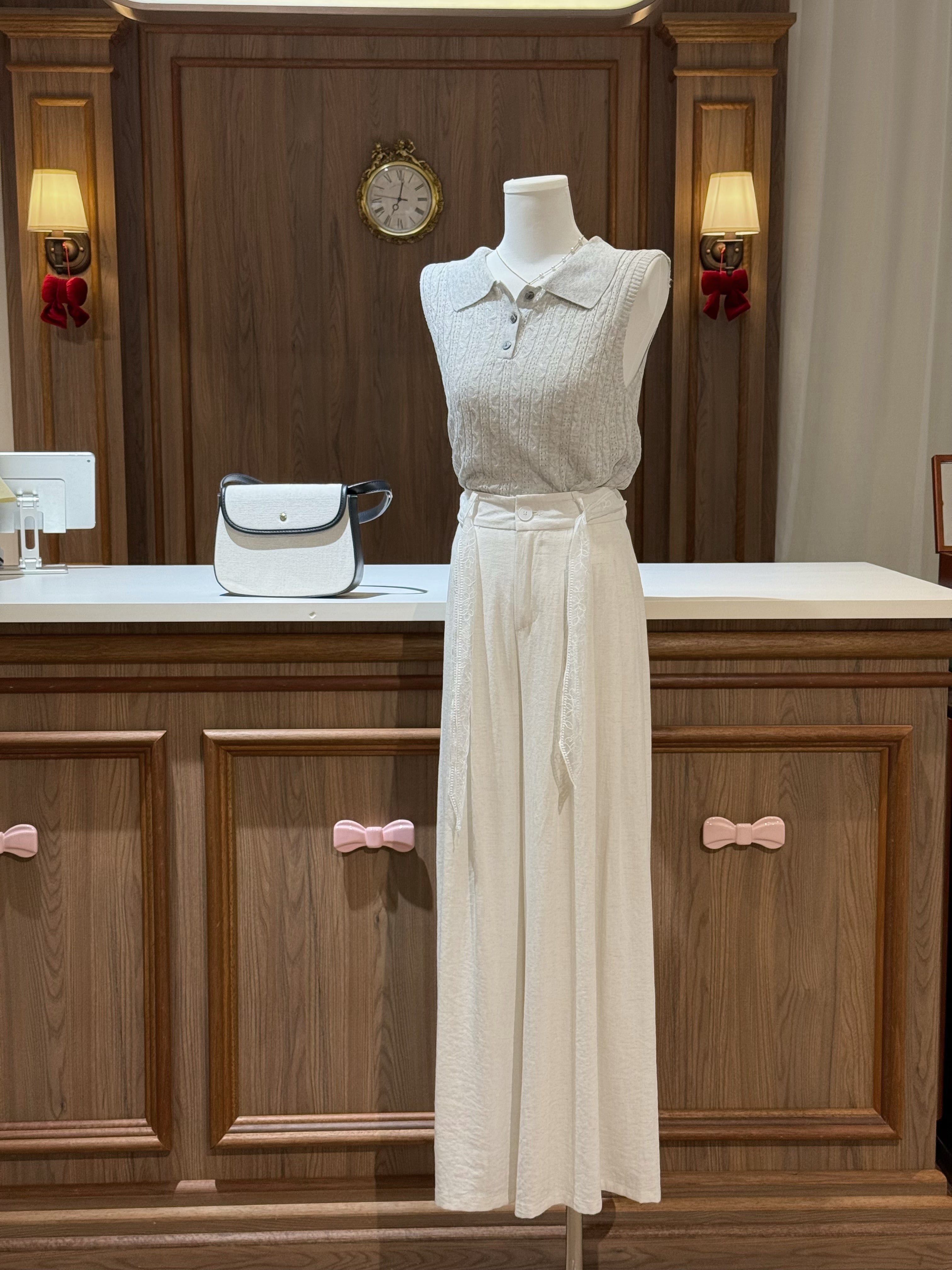 Mannequin wearing a light-colored outfit with a white handbag on a wooden counter.