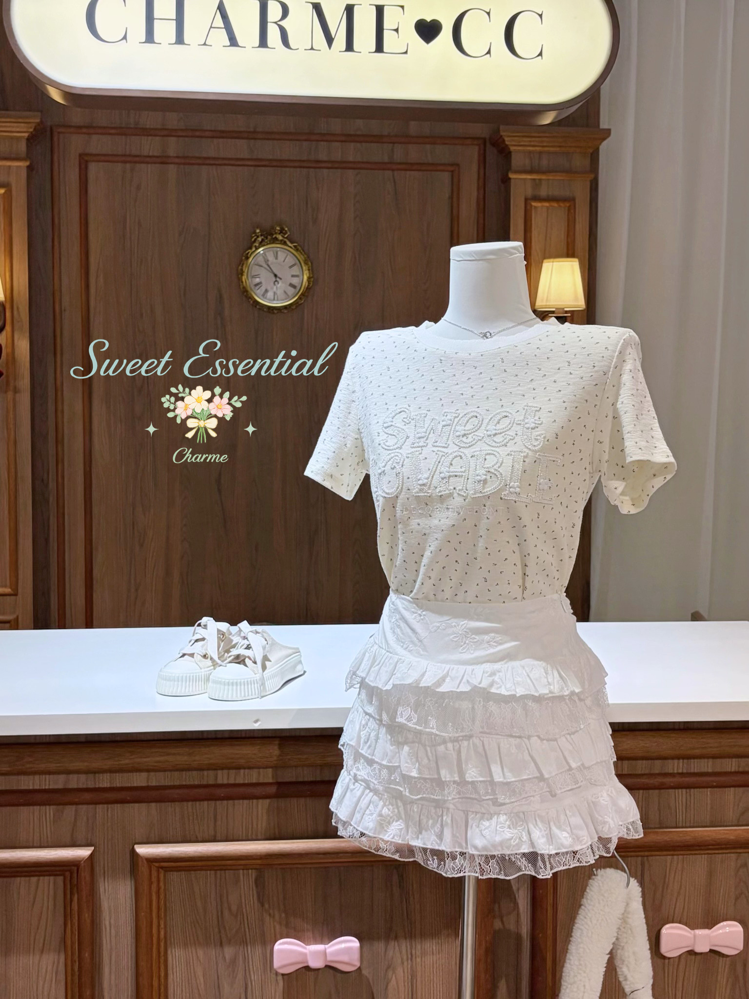 White lace dress on a mannequin in front of a wooden wall with 'Charme' branding.