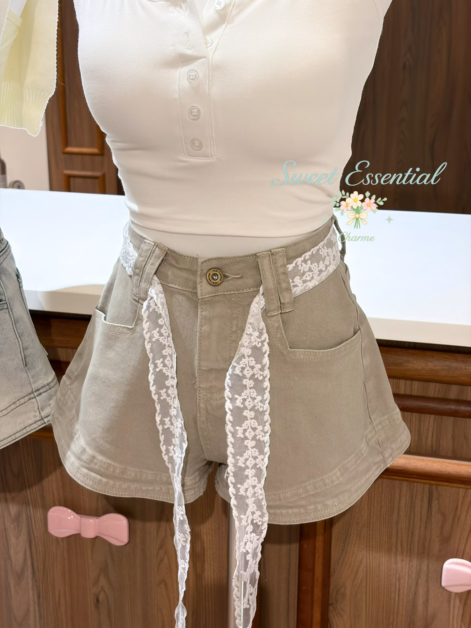 Person wearing beige shorts with lace trim and a white top, standing in front of a wooden cabinet.